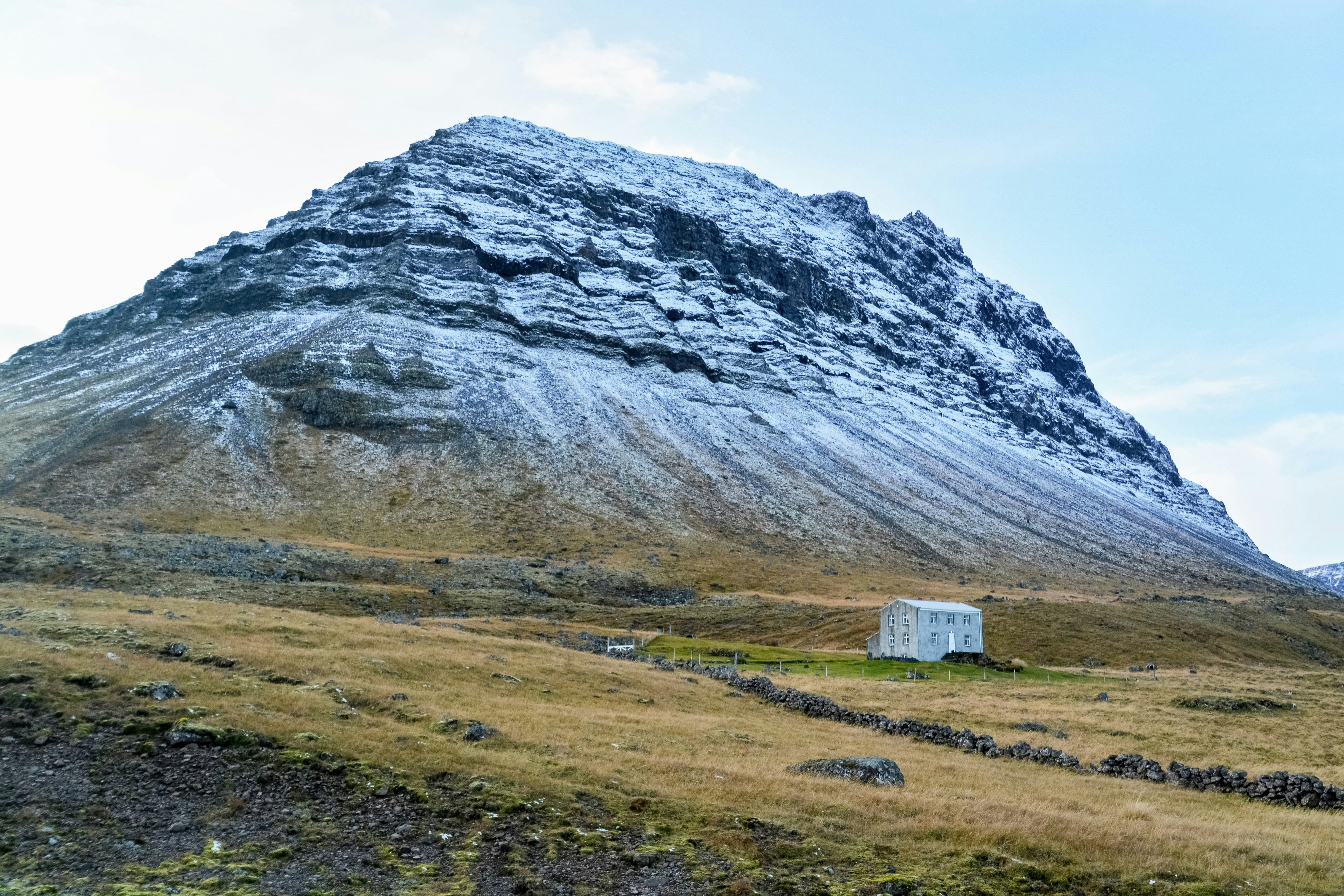 white and brown wooden house on green grass field near gray rocky mountain during daytime